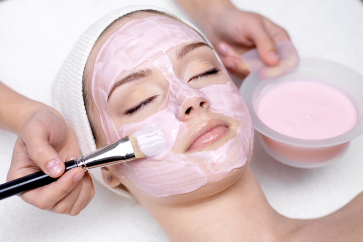 Person receiving a pink facial mask treatment at a spa.