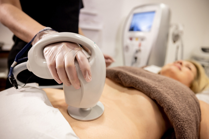 A beautician performs a body contouring treatment with a handheld device.