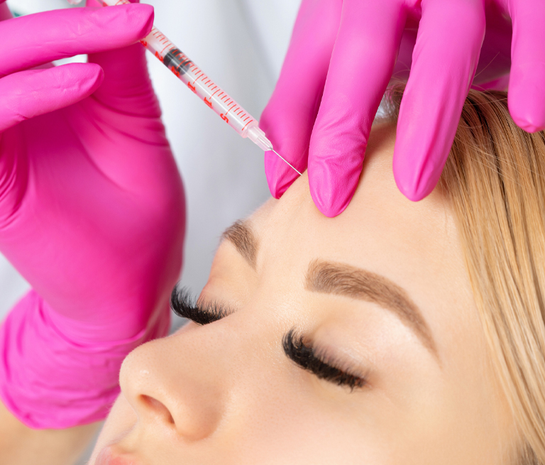 Injection of a syringe into a woman's forehead, wearing pink gloves.