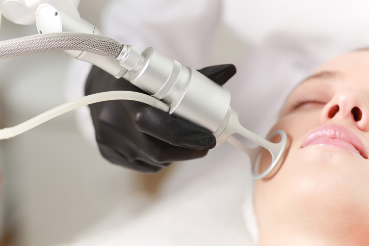 A woman receiving a laser facial treatment from a professional wearing gloves.