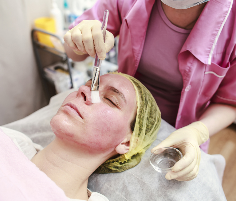 Facial treatment with brush application on a woman's face in a spa setting.