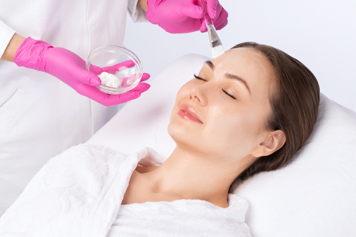 A woman receiving a facial treatment with a white cream applied on her forehead.