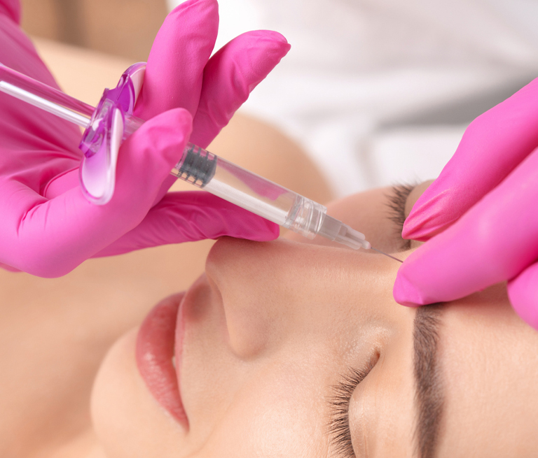 Pink-gloved professional injecting filler into woman's nose for cosmetic treatment.