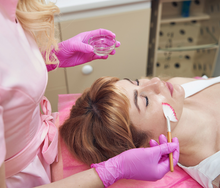 Woman receiving facial treatment with brush and pink gloves.
