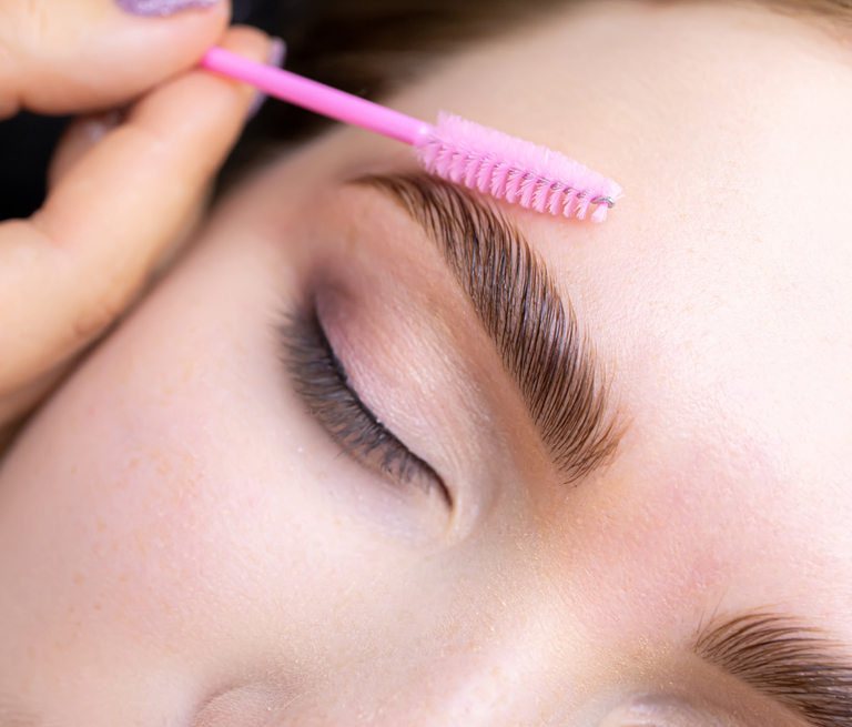 Person getting eyebrows brushed with a pink spoolie brush.