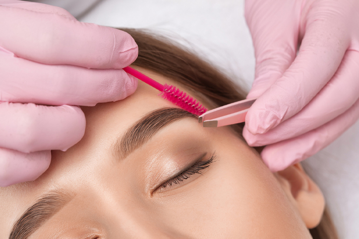 Grooming eyebrows with tweezers and brush in a beauty salon.
