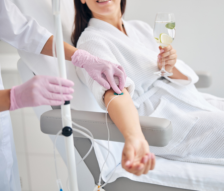 Woman receiving IV therapy while holding a drink in a spa setting.