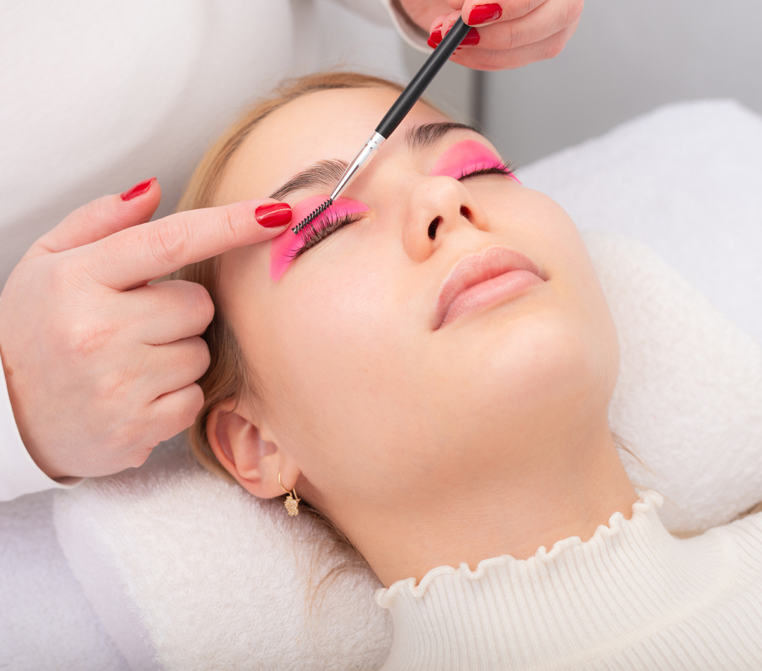 A woman receiving eyelash treatment with pink pads and brush.
