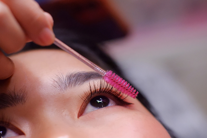 Applying mascara with pink brush to eyelashes close-up.