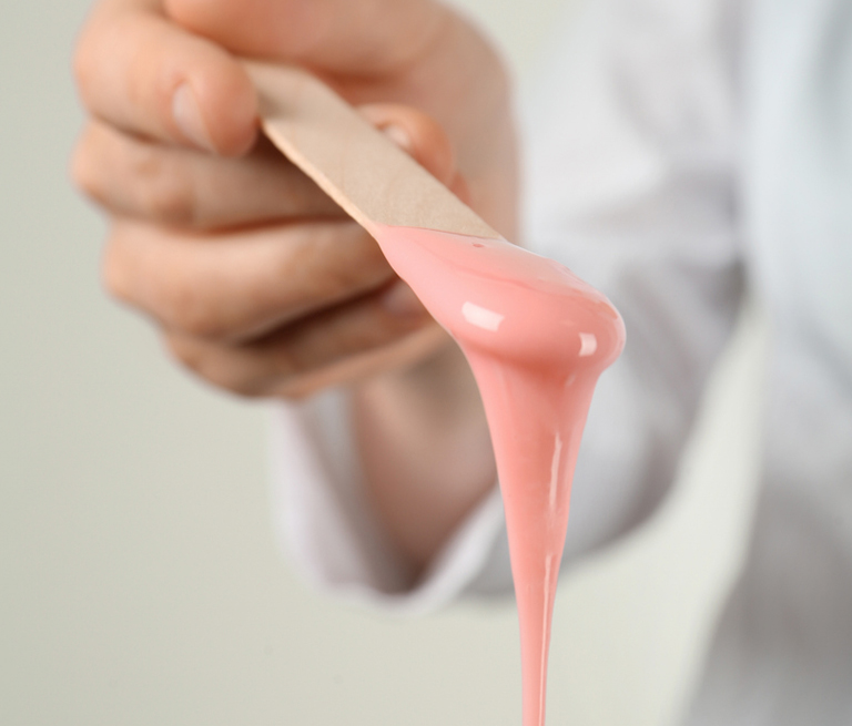 A person holding a wooden stick with pink waxing paste.