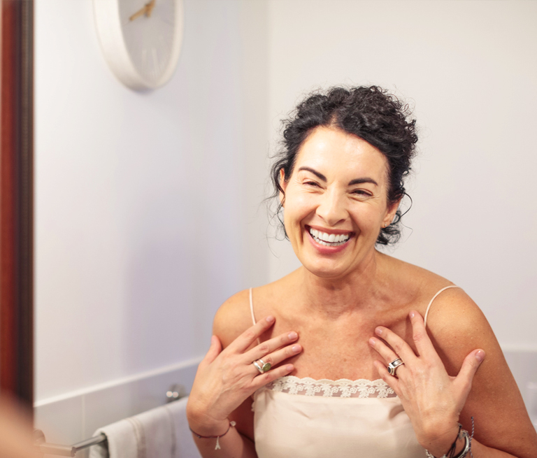 Woman smiling joyfully in front of a bathroom mirror.