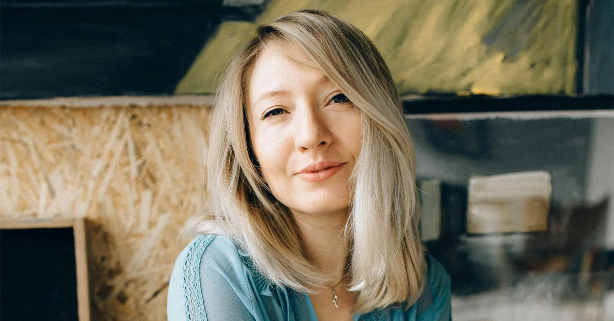 A woman with blonde hair in a blue shirt against a textured background.