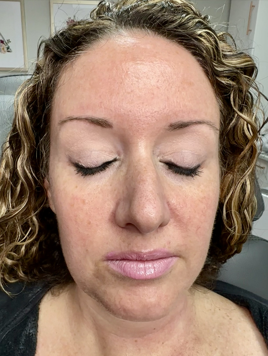 Woman with closed eyes showing natural makeup and curly hair.