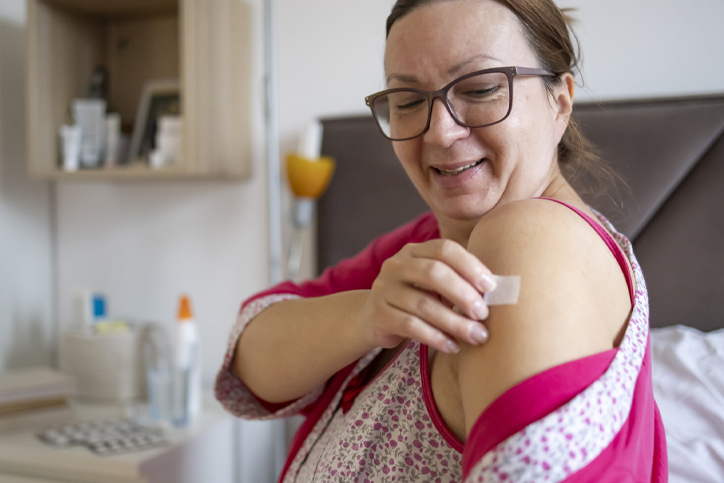 Woman applying a bandage to arm after injection, smiling.