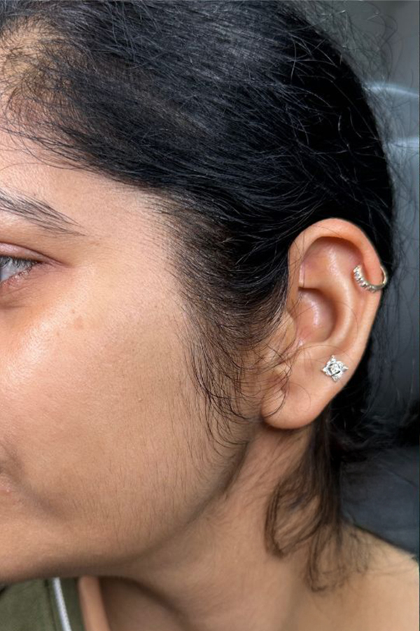Close-up of a person's ear with multiple earrings, including a hoop and a stud.