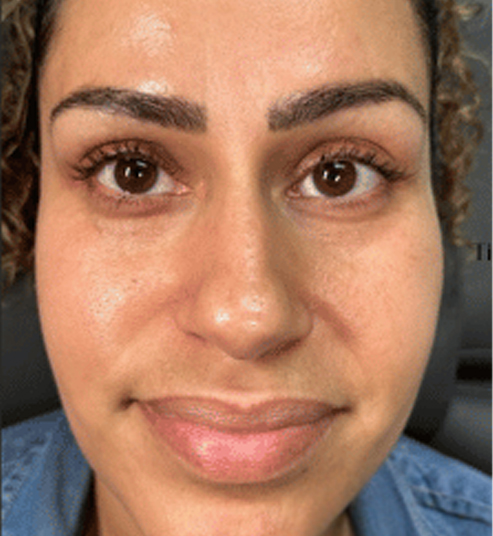 A person with curly hair and expressive eyebrows smiling softly.