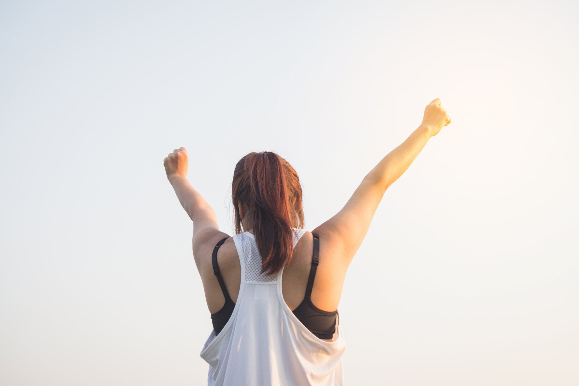 Woman raising her arms in triumph against a clear sky.